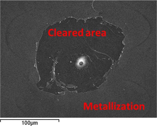 Figure 20. SEM image shows a pin hole in the middle, with a cleared area around it and a typical metallized surface in a de-processed film-capacitor.